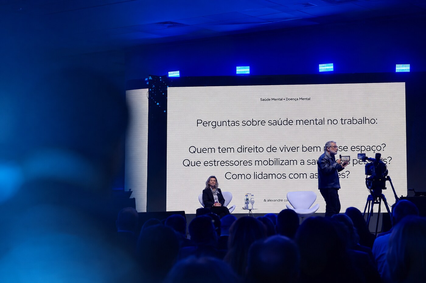 Palestra sobre saúde mental no 28º EESCON, com palco e participantes sob iluminação azul